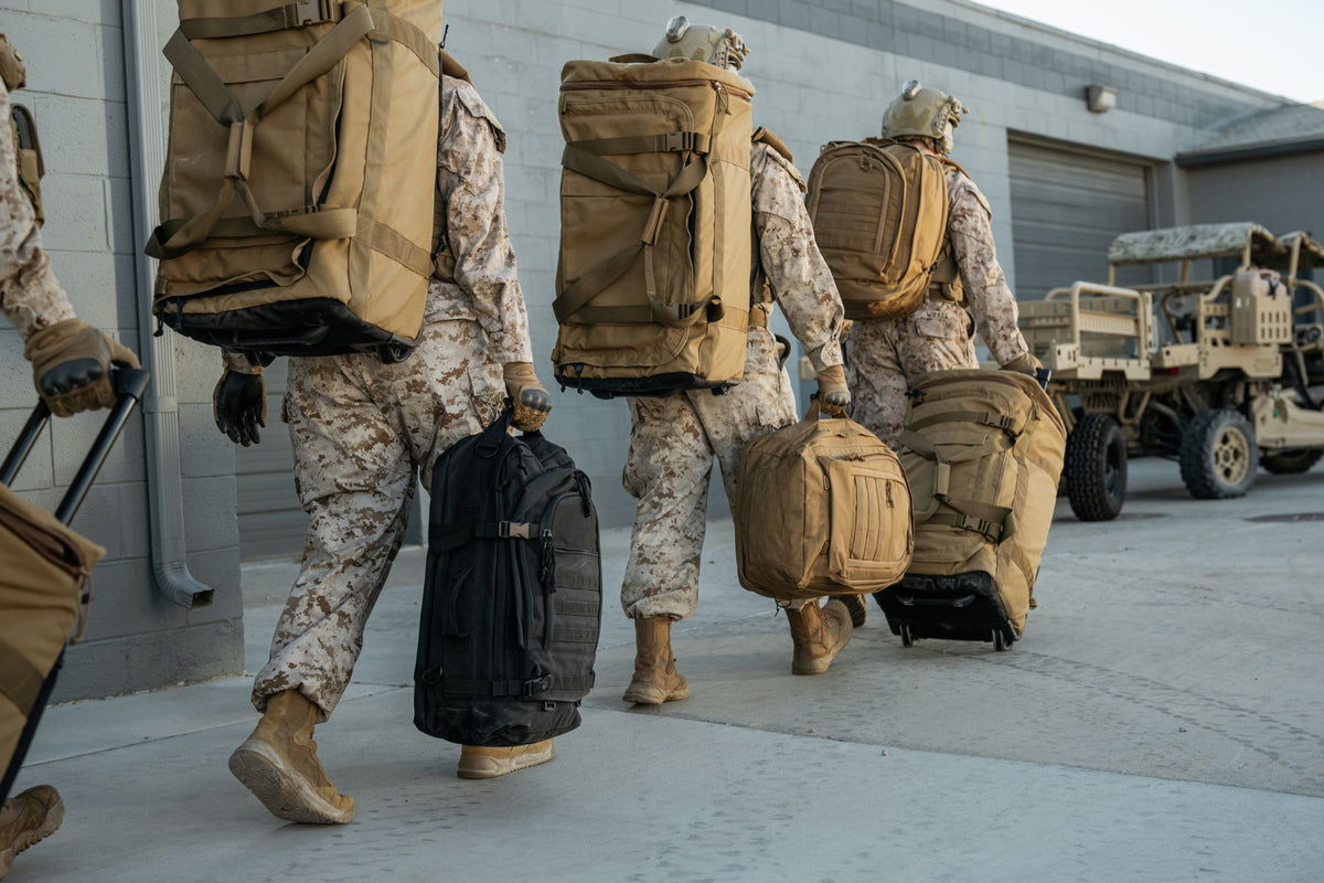Three soldiers in camouflage uniforms with large backpacks walking together.