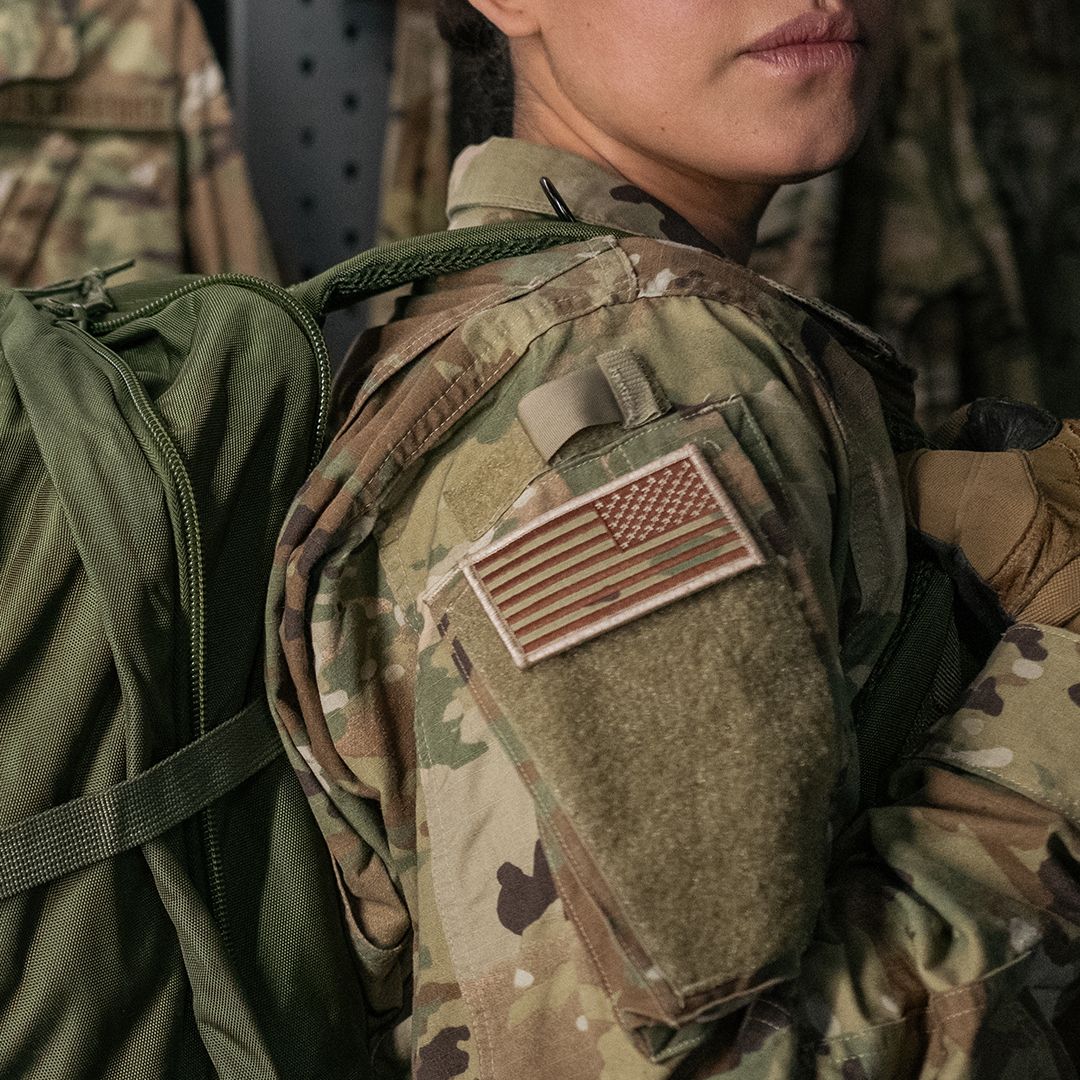backpack on woman's right shoulder featuring an American flag patch wearing US Army gear