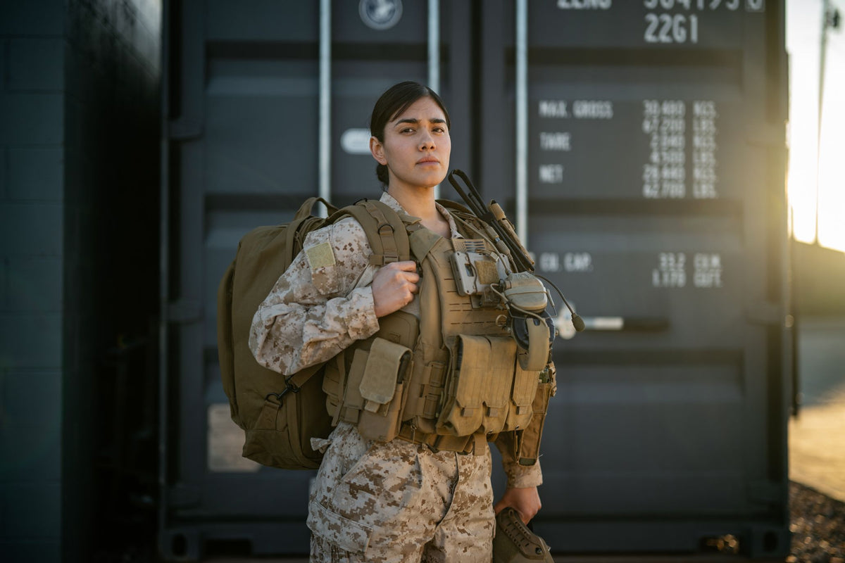 Person in military uniform with gear standing in front of a large electronic display board.