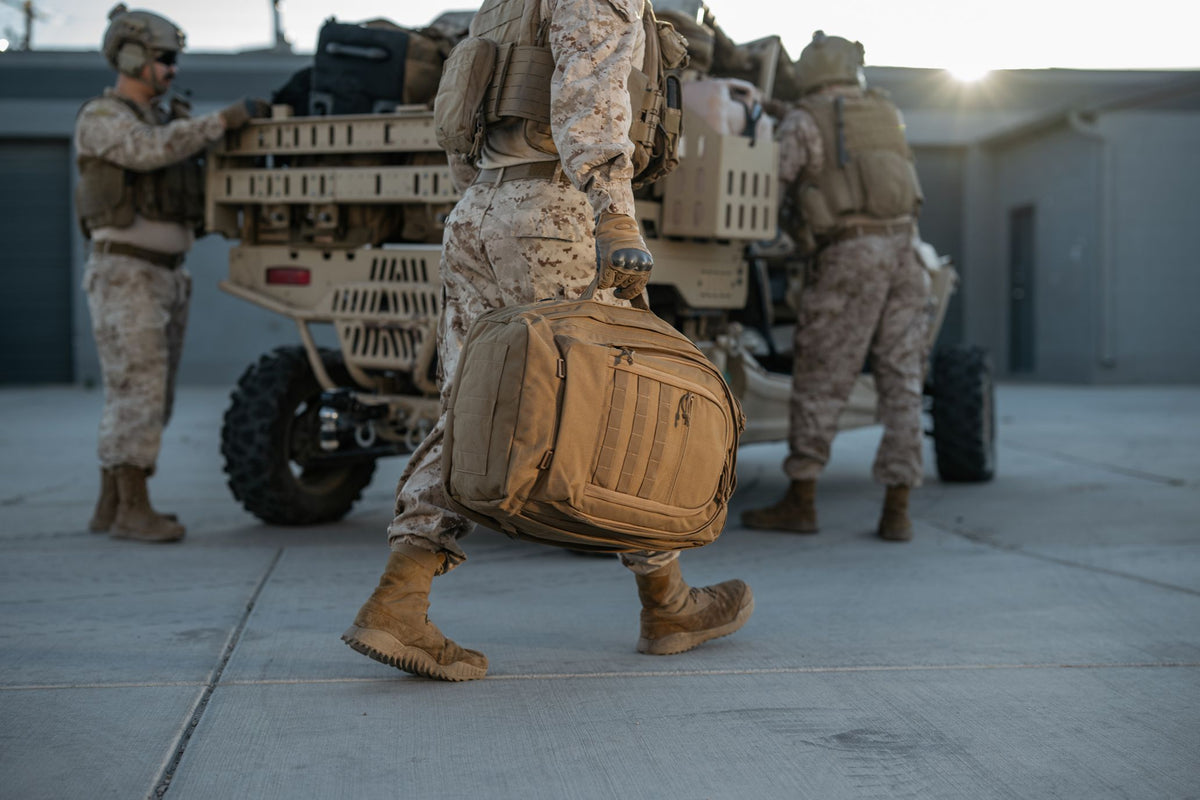 Military personnel carrying a tactical deployment bag during field operations
